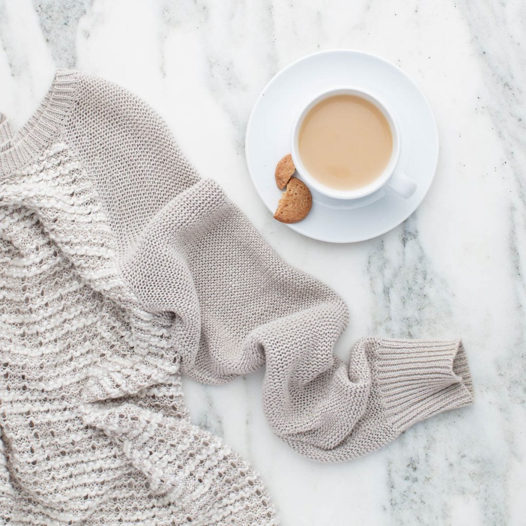 Image of a cup of coffee in a white cup, along with a off while color scarf on white carpet.